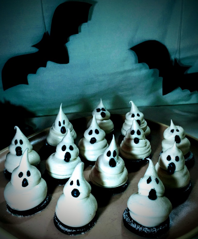 The marshmallow ghosts, with droopy black icing features, casting long shadows, with the silhouettes of bats in the background.
